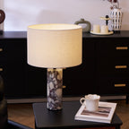 Clérachic marble table lamp on a light wood side table, with a ceramic vase of branches and a cup on a book nearby.