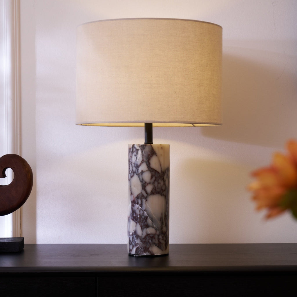 A spray of orange and white flowers blurs in the foreground of the Clérachic marble lamp on its dark sideboard.