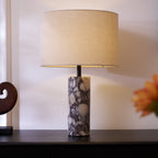 A spray of orange and white flowers blurs in the foreground of the Clérachic marble lamp on its dark sideboard.