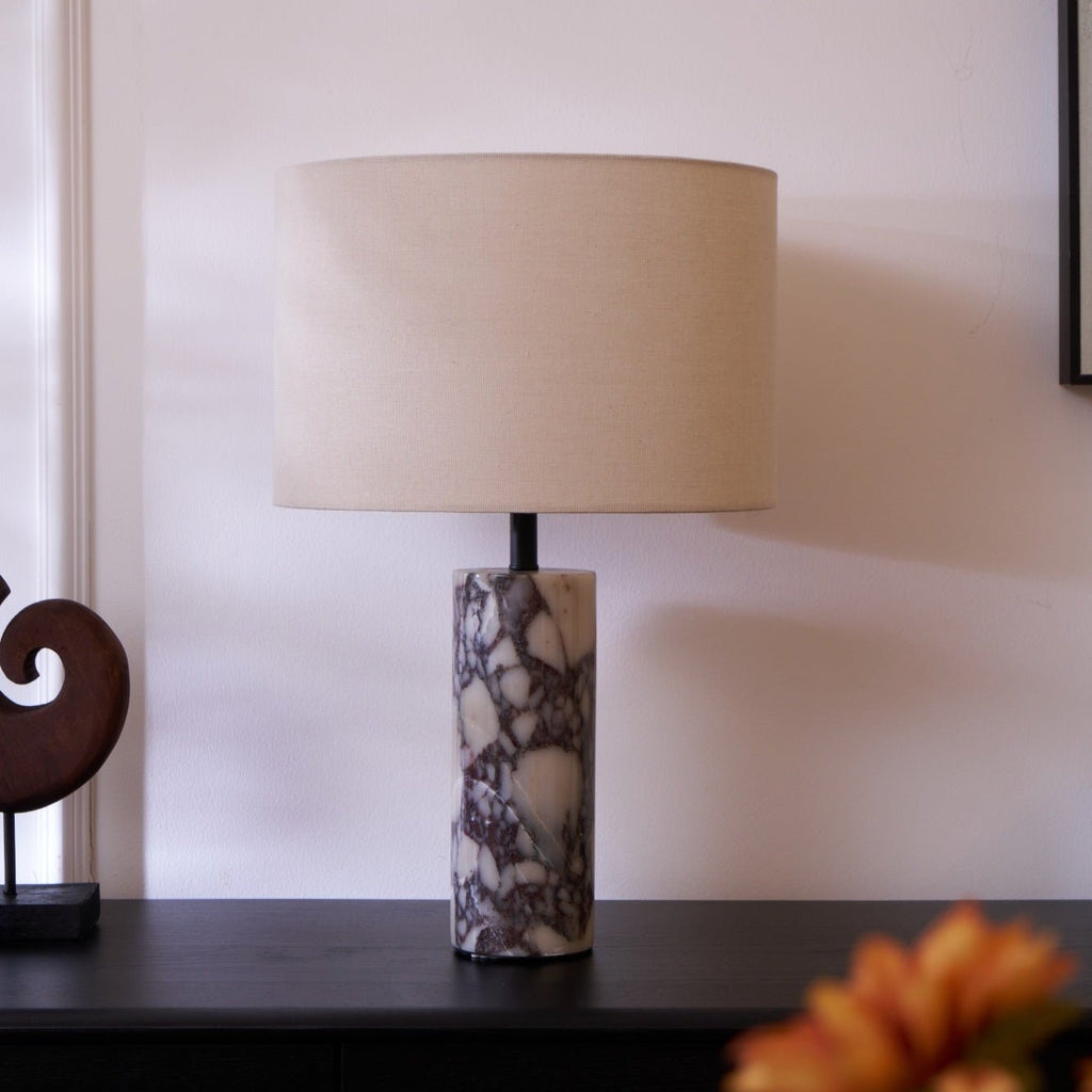 Clérachic marble table lamp beside a black leather chair, an orange flower soft-focused in the foreground below it.