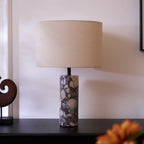 Clérachic marble table lamp beside a black leather chair, an orange flower soft-focused in the foreground below it.