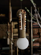 Clérachic wall sconce shown up close against a dark glass cabinet, its mixed stone beads lit beside a bare branch.