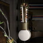 Clérachic wall sconce in close-up against a dark bookshelf backdrop, mixed stone beads glowing beside bare branches.