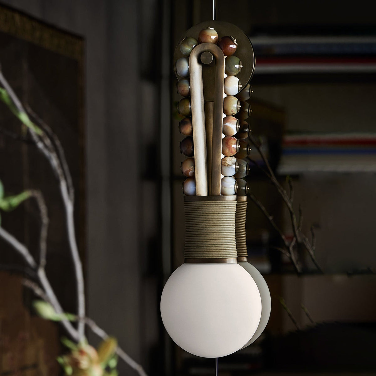 Clérachic wall sconce in close-up against a dark bookshelf backdrop, mixed stone beads glowing beside bare branches.