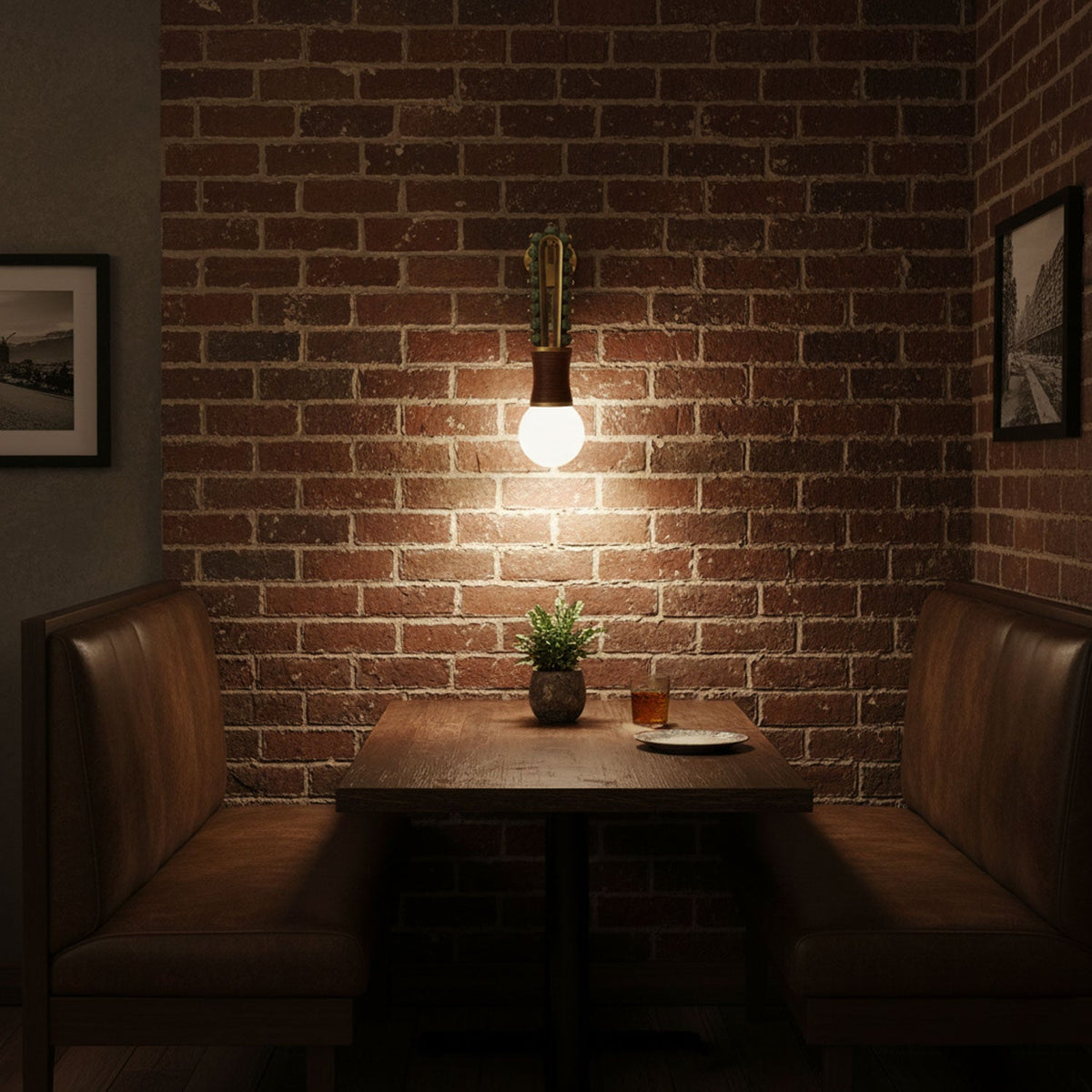 Clérachic wall sconce lit above a leather booth table against an exposed brick wall, with a small plant on the table.