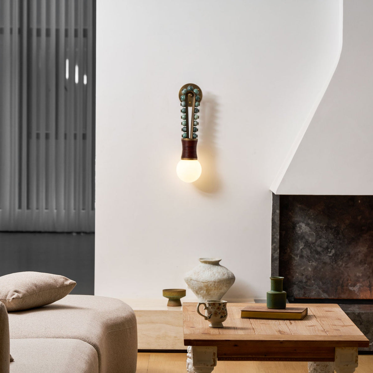 Clérachic wall sconce lit beside a fireplace in a modern living room, with a sofa and coffee table nearby.
