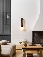 Clérachic wall sconce lit on a white wall in a living room, near a sofa and a coffee table with books and a vase.