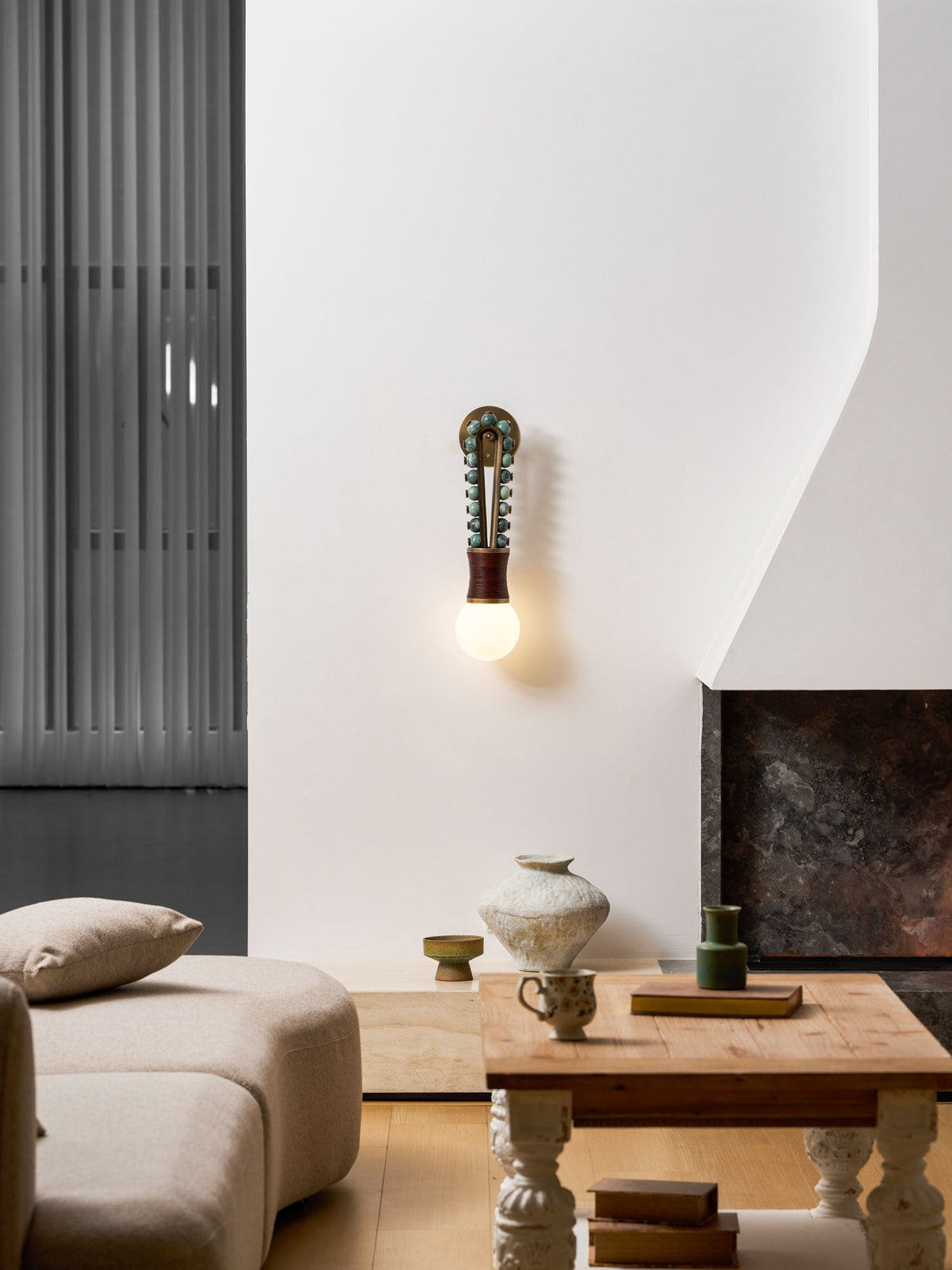 Clérachic wall sconce lit on a white wall in a living room, near a sofa and a coffee table with books and a vase.