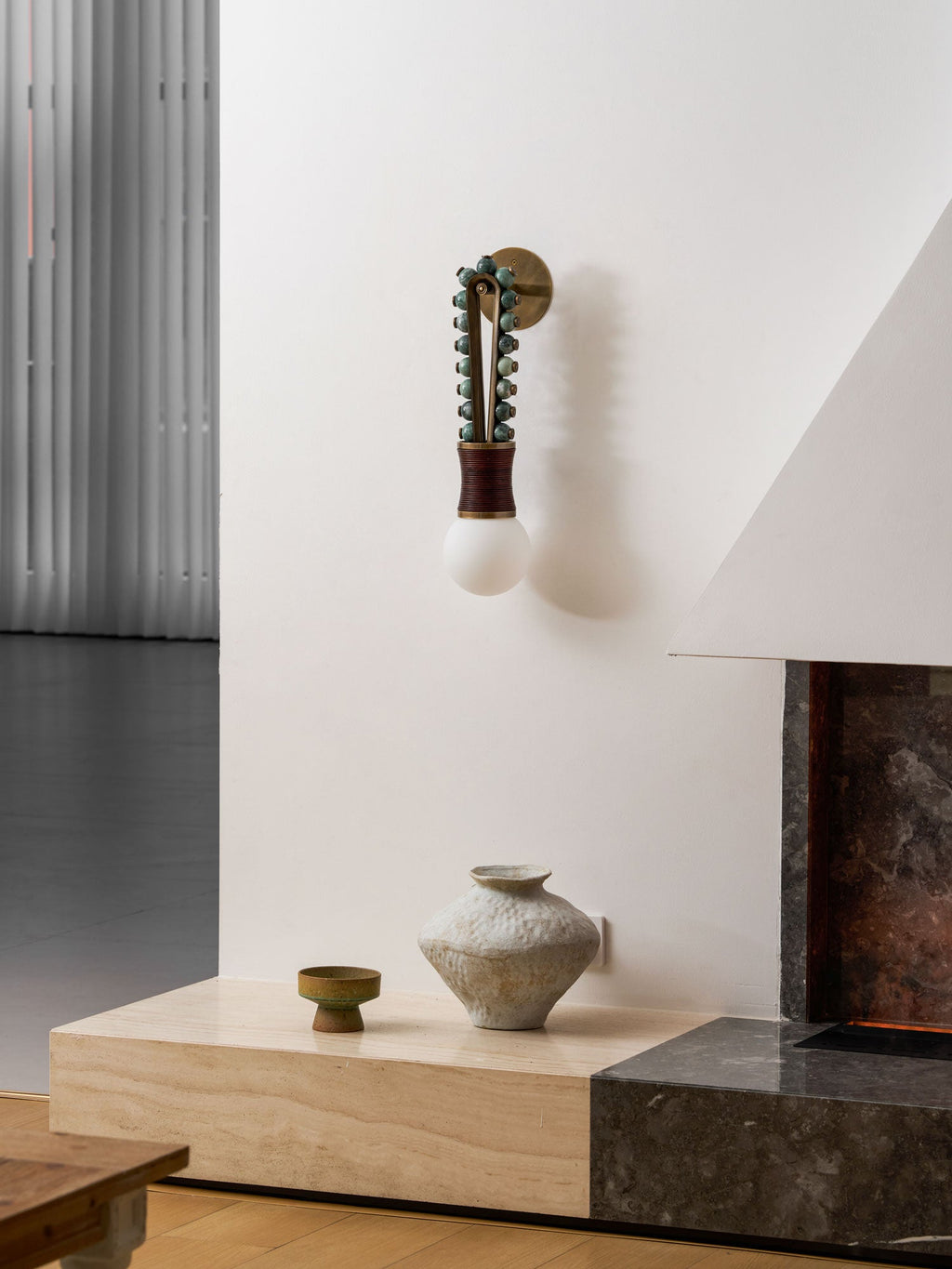 Sage-green beads and a maroon-wrapped base glow on a Clérachic wall sconce near a white fireplace corner.