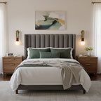 A channel-tufted grey headboard sits between two lit Clérachic wall sconces in a quiet bedroom.