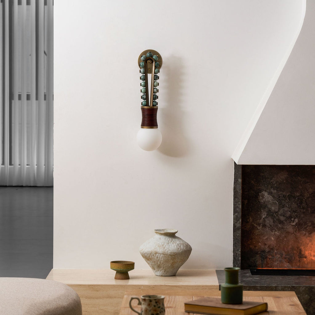 A ceramic vase sits on the hearth beside a fireplace, lit by a Clérachic wall sconce on the white wall.