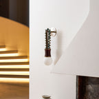 Clérachic wall sconce mounted beside a curved staircase, its pale globe unlit against the white wall and stairwell glow.