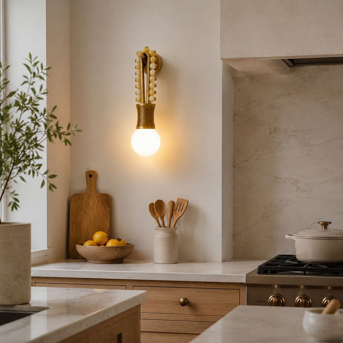 A wooden cutting board and fruit bowl sit near the stove, lit by a Clérachic wall sconce in the kitchen corner.