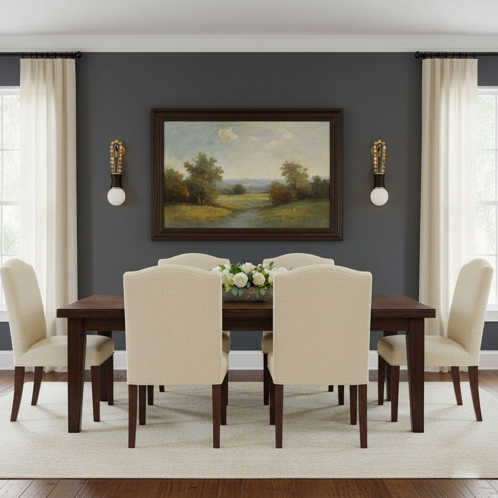 The dining table sits beneath a framed landscape painting, lit either side by two Clérachic wall sconces in a grey-blue room.