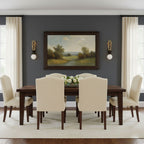 The dining table sits beneath a framed landscape painting, lit either side by two Clérachic wall sconces in a grey-blue room.
