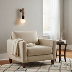 Clérachic wall sconce lit beside a cream armchair with a folded throw, near a window with sheer white curtains.