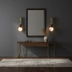 A mirror above a console table sits between two lit Clérachic wall sconces in a dark blue-grey room.