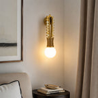 Clérachic wall sconce lit in a living room corner beside a cream sofa and a dark side table stacked with books.