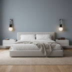 Either side of a low bed, two Clérachic wall sconces glow softly against a dusty-blue bedroom wall.