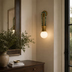 Clérachic wall sconce lit beside an entryway mirror, with a vase and dresser below it near the front door.