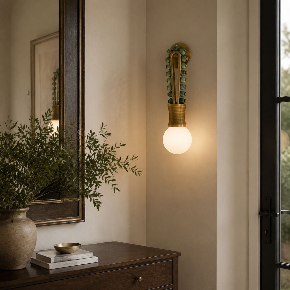 Clérachic wall sconce lit beside an entryway mirror, with a vase and dresser below it near the front door.