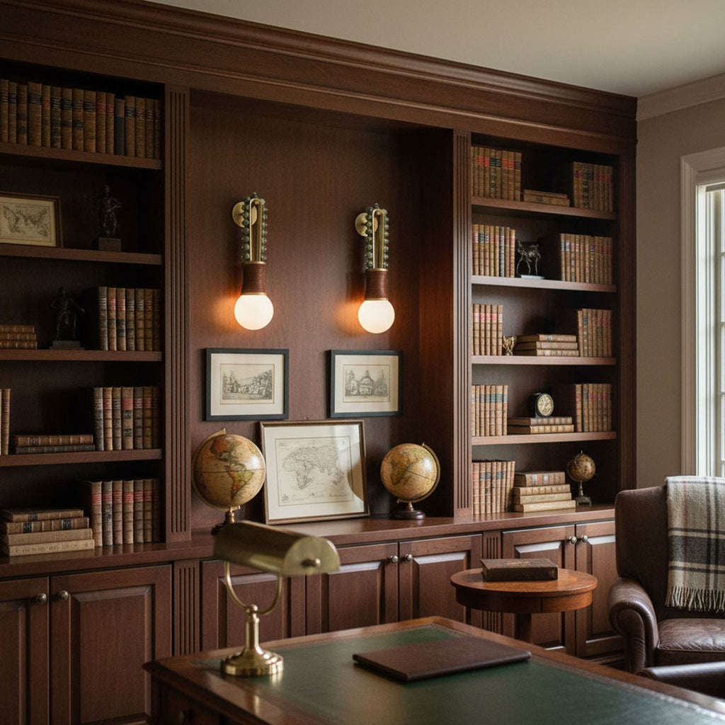 Two Clérachic wall sconces lit either side of a bookshelf nook, glowing above a wood desk in a panelled study.