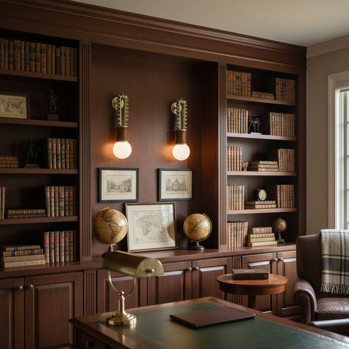 Two Clérachic wall sconces lit either side of a bookshelf nook, glowing above a wood desk in a panelled study.