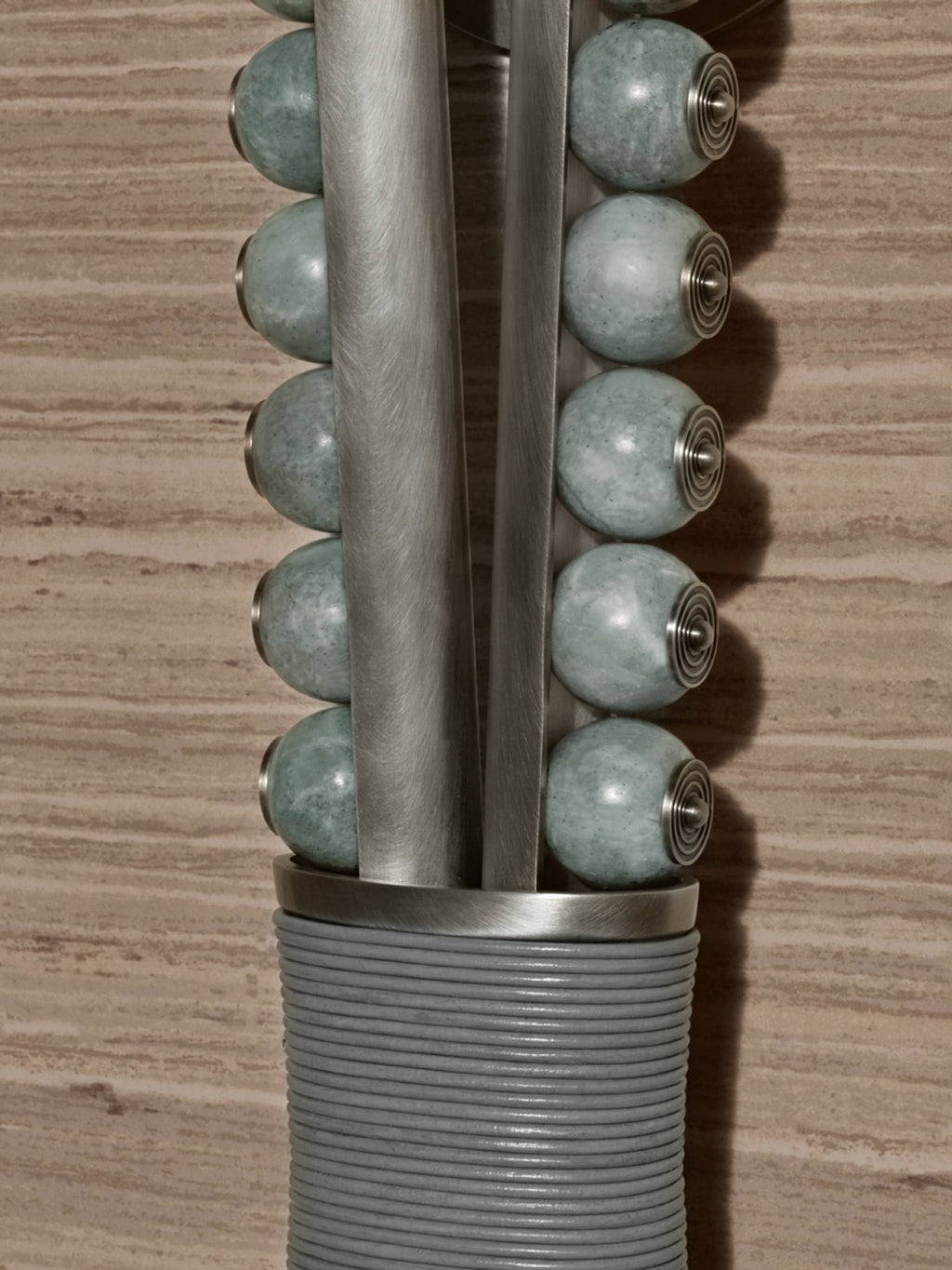 Close-up of a Clérachic wall sconce's pale sage stone beads on a metal rod with brass end caps, against a wood-grain wall.