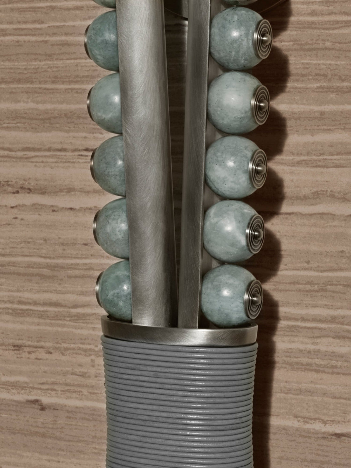 Close-up of a Clérachic wall sconce's pale sage stone beads on a metal rod with brass end caps, against a wood-grain wall.