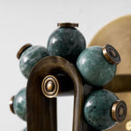 Close-up of a Clérachic wall sconce's dark green marbled stone spheres set in brass caps along a bronze frame.