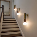 Three Clérachic wall sconces lit along a staircase hallway, their glow reflected in a large mirror at the top.