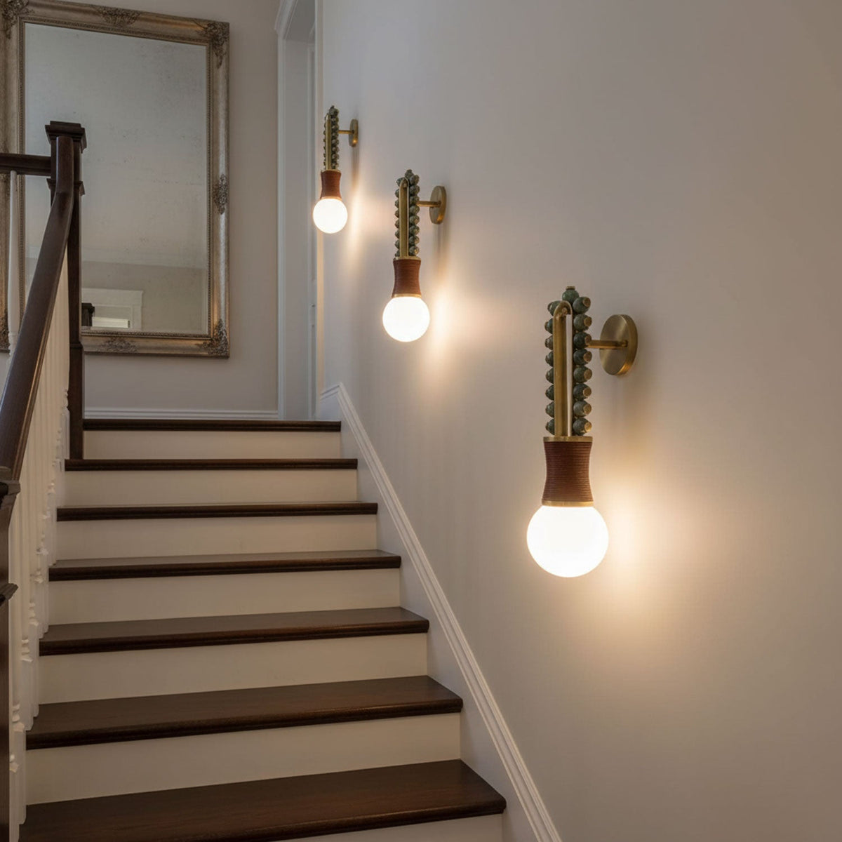 Three Clérachic wall sconces lit along a staircase hallway, their glow reflected in a large mirror at the top.