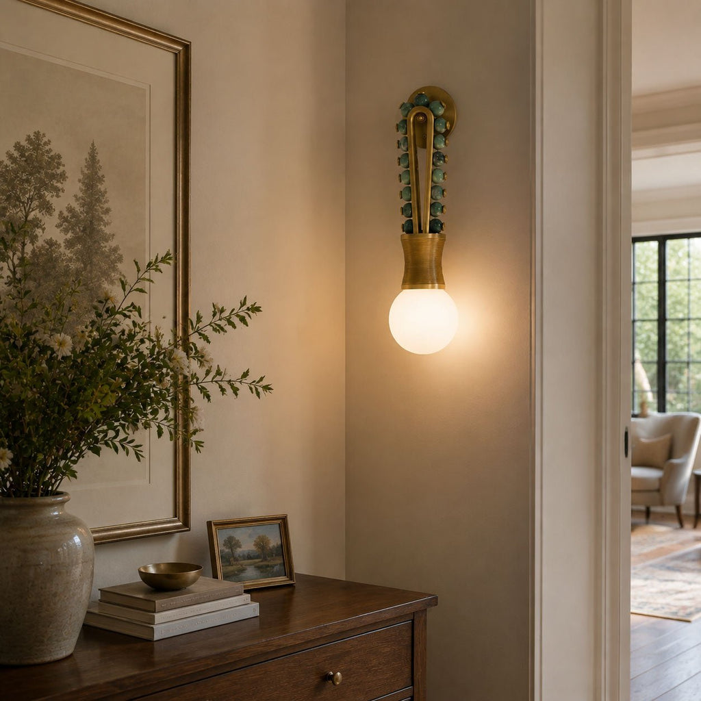 Clérachic wall sconce lit in a hallway beside a framed botanical print, above a wooden chest of drawers.