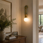 Clérachic wall sconce lit in a hallway beside a framed botanical print, above a wooden chest of drawers.