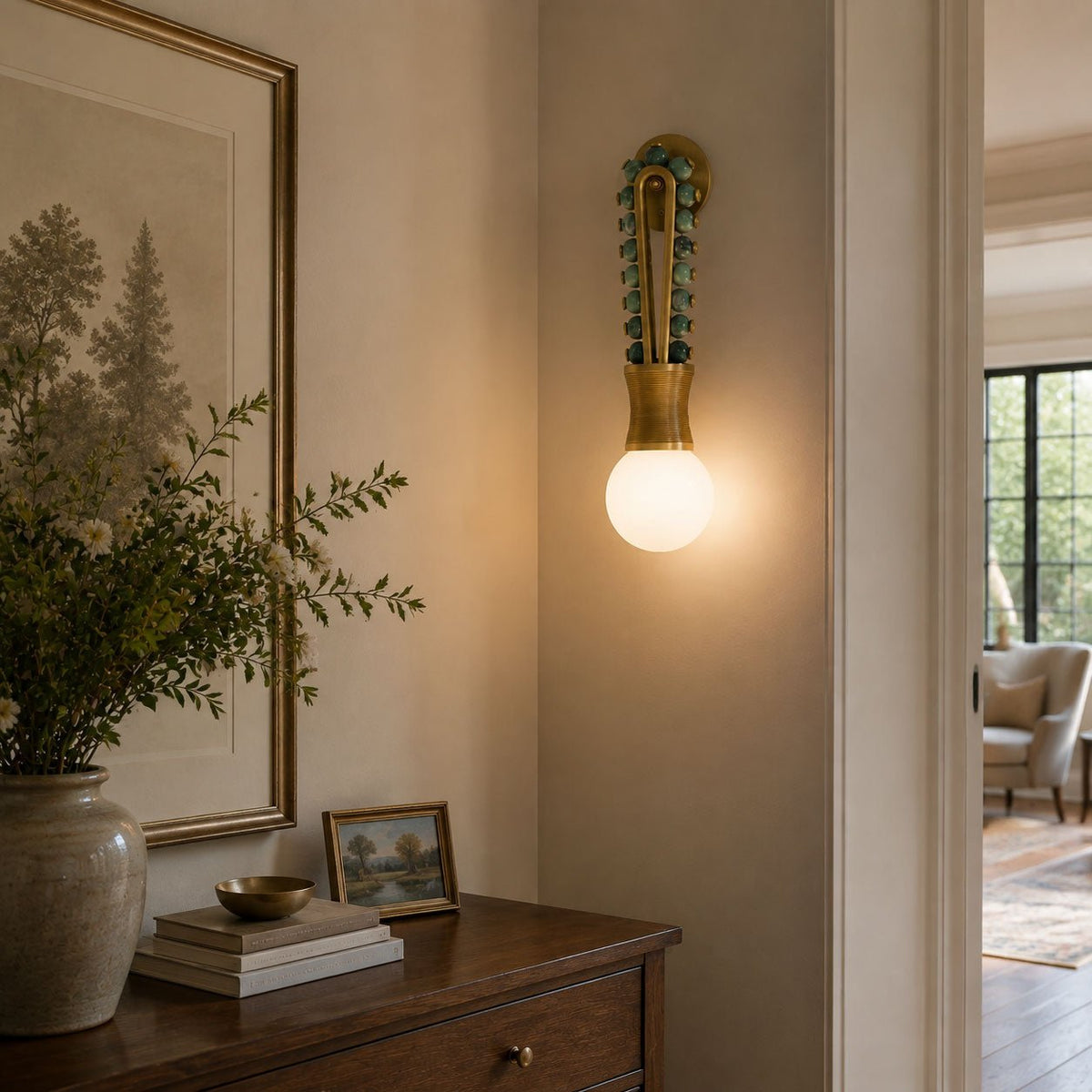 Clérachic wall sconce lit in a hallway beside a framed botanical print, above a wooden chest of drawers.