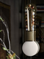 Clérachic wall sconce in close-up against a dark backdrop, mixed stone beads glowing warmly beside a bare branch.