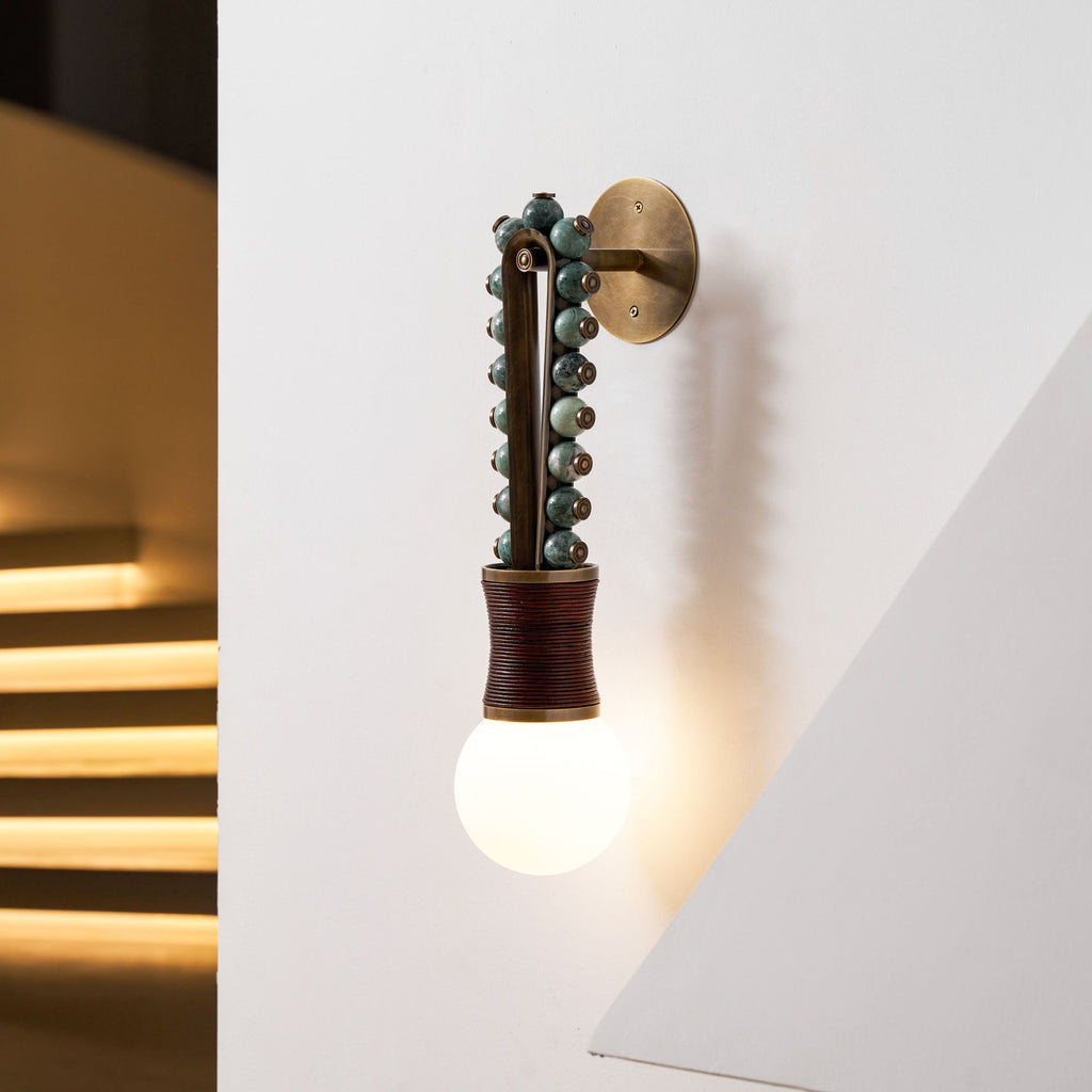 Clérachic wall sconce glowing warmly in a stairwell corner, its light spilling across the lit wooden steps below.