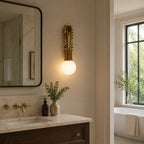 Clérachic wall sconce lit above a marble bathroom vanity, beside a window and a freestanding tub.