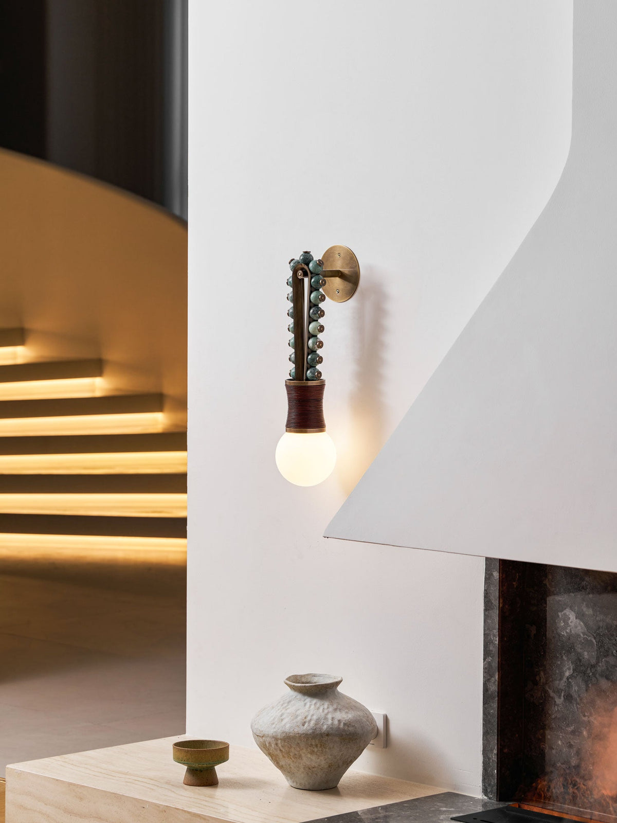 Clérachic wall sconce lit near a curved staircase, with warm light spilling across the wooden steps below.