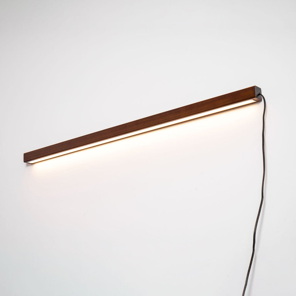 Pine wood disc wall light shown lit against a neutral wall