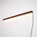 Pine wood disc wall light shown lit against a neutral wall