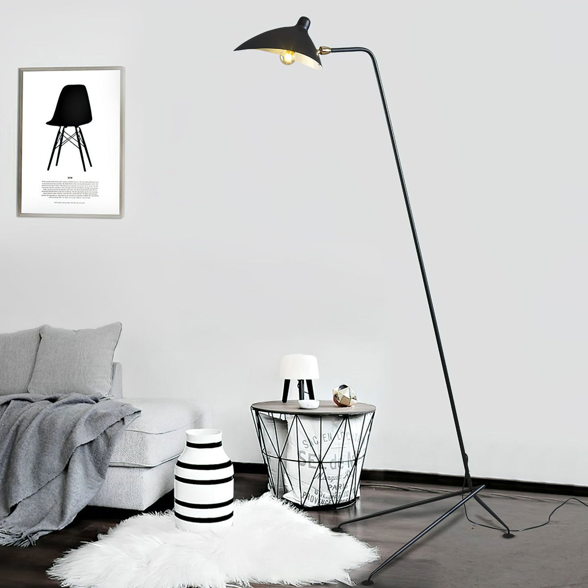 Lit and glowing, this Clérachic floor lamp stands beside a grey sofa, a striped side table, and a framed print.