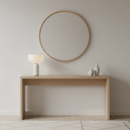 A white marble Clérachic sphere lamp sits on an oak console table beneath a round mirror, two small birds nearby.