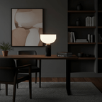Clérachic's sphere table lamp lit on a dark wood desk in a moody study, framed art and bookshelves behind.