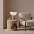 Clérachic's grey marble sphere lamp lit on a wooden side table beside a bouclé armchair and a small ceramic vase.