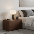 The dark red marble base of this Clérachic table lamp lit on a wooden nightstand beside a pillow-stacked bed.