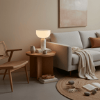 Clérachic's white marble sphere lamp glows on a round wooden side table between a cream sofa and a woven chair.