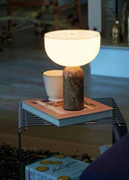 Clérachic's marble-based table lamp lit on a stack of books on a wire side table, a teacup set beside it.