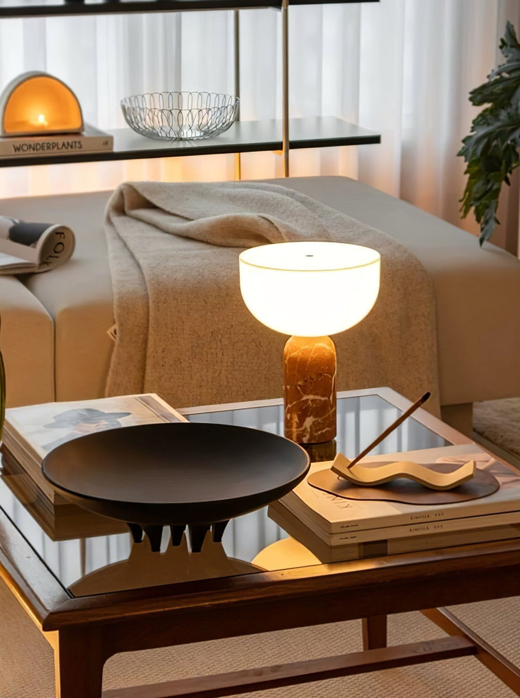 Clérachic's sphere table lamp lit on a wooden coffee table beside a stack of magazines and a black dish.