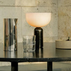 Clérachic's dark marble table lamp lit on a reflective black table beside a metallic pitcher and glass tumbler.